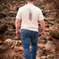 Man walking on rocky path near stream.