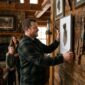 Man hangs artwork in rustic home, family watches.