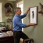 Man hanging framed artwork in study